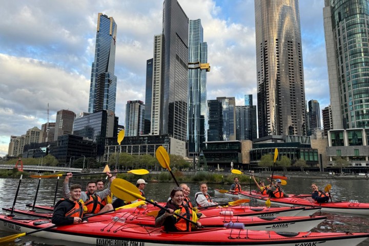 Group kayaking on river with city skyscrapers in background.