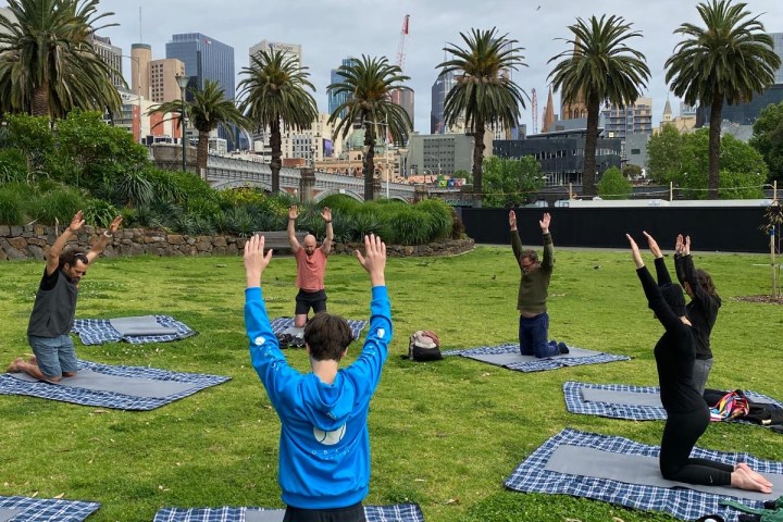 Group doing outdoor yoga on mats in a park with palm trees.