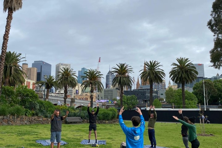 Group doing yoga outdoors on mats, city skyline in background.