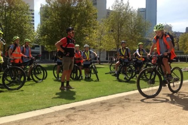 Group of cyclists wearing helmets and safety vests, gathered in a park.