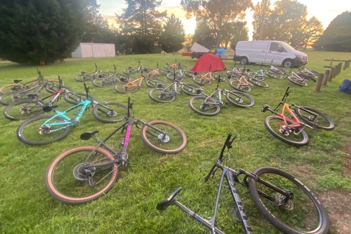 Several bikes on grass with a van and tent in the background at sunset.