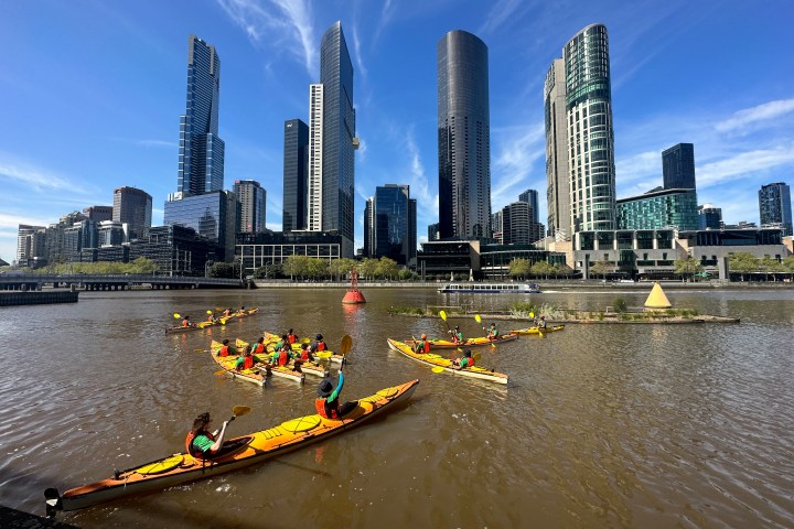 Kayakers on a river with a city skyline and modern skyscrapers in the background.